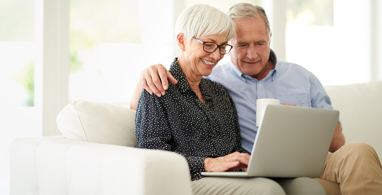 Senior couple sitting on a couch and looking at a laptop